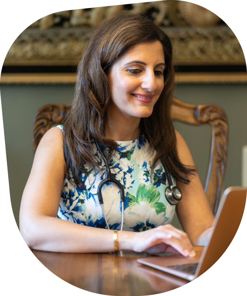 Dr. Sarita Mahtani smiling while working on a laptop, representing compassionate functional medicine care in a professional clinical setting